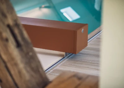 Boîtier rectangulaire marron fixé sur un rail en métal, posé sur un sol en bois clair, avec une piscine en arrière-plan.