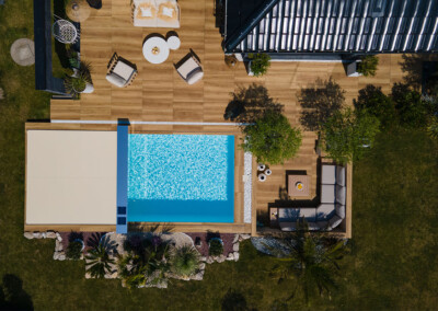 DreamHomeFamily Vue aérienne d’une piscine haut de gamme équipée d’une couverture Coverseal beige, intégrée dans une terrasse design avec salon de jardin moderne.