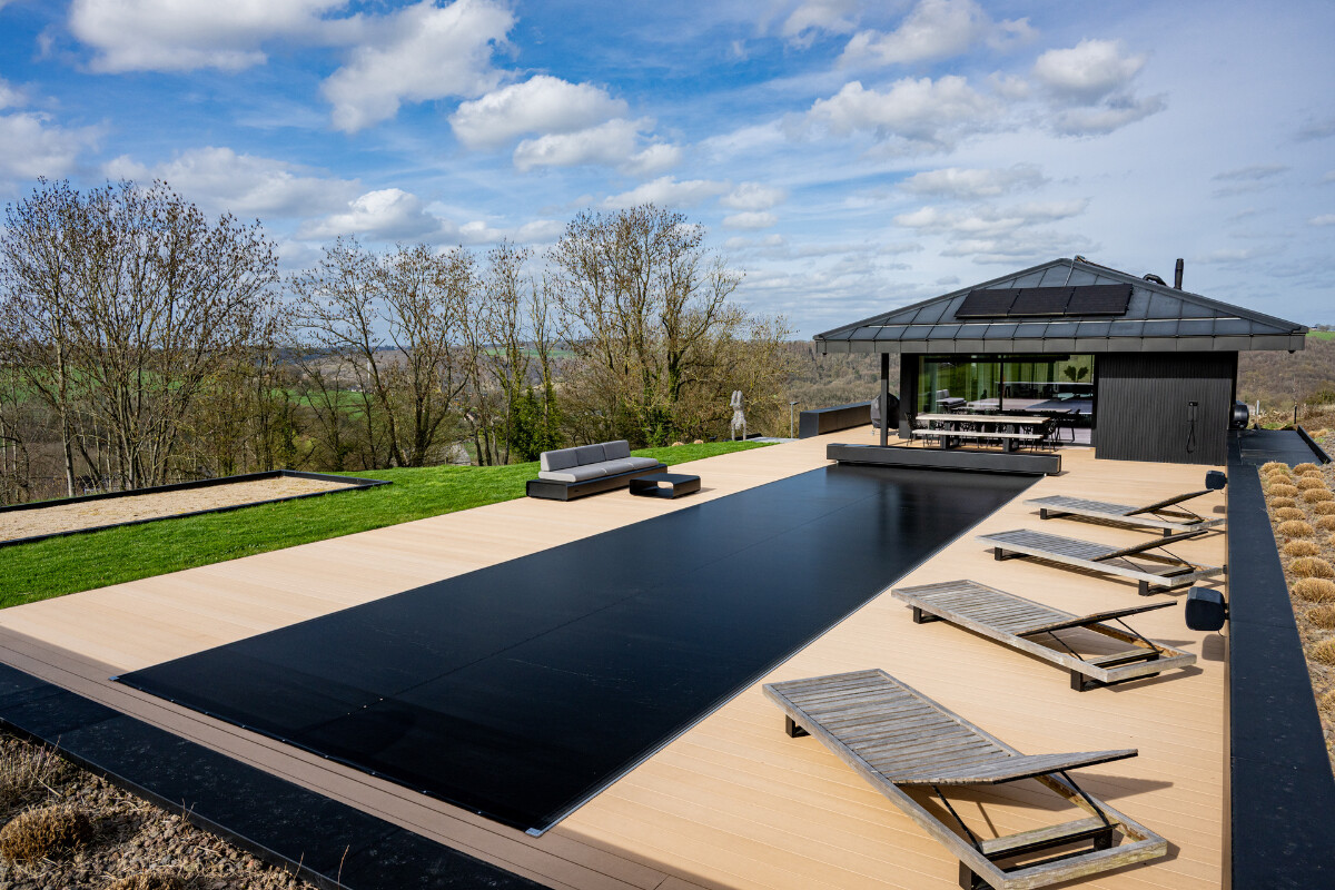 Gros plan sur l'habillage de la Coverseal grise au bord de la piscine, avec en arrière-plan les transats et la maison en pierre.